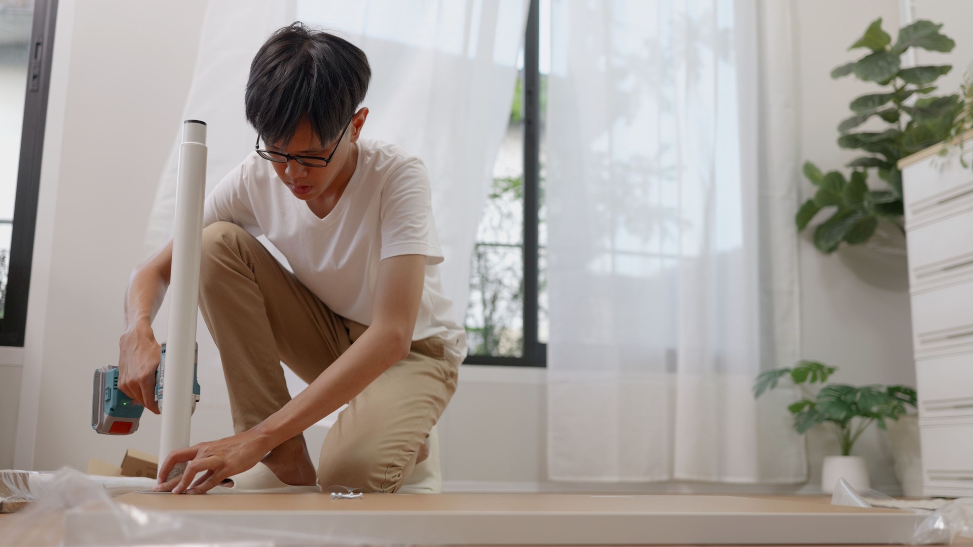 Asian man unboxing and assembling new table in the living room.